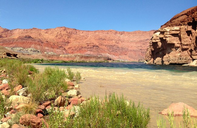 Murky brown water meets clear blue water inside a steep canyon