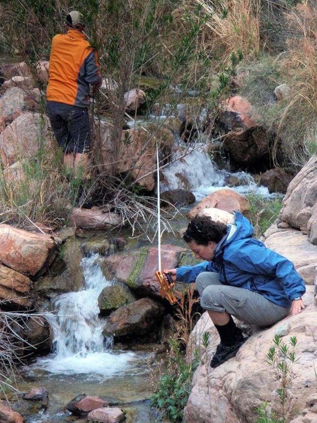 Two people measuring a section of a boulder strewn stream with tape.