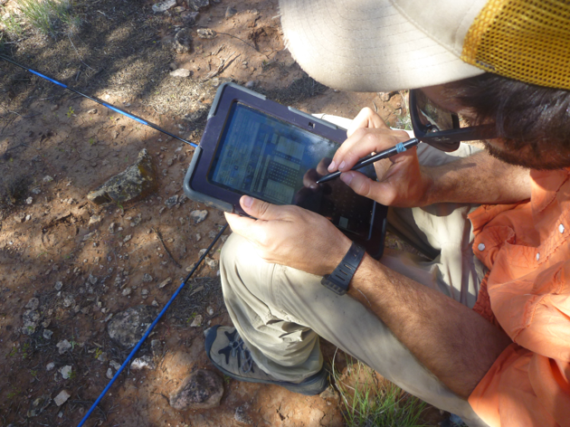 Collecting field data. Man in orange shirt and beige pants entering data on a tablet.