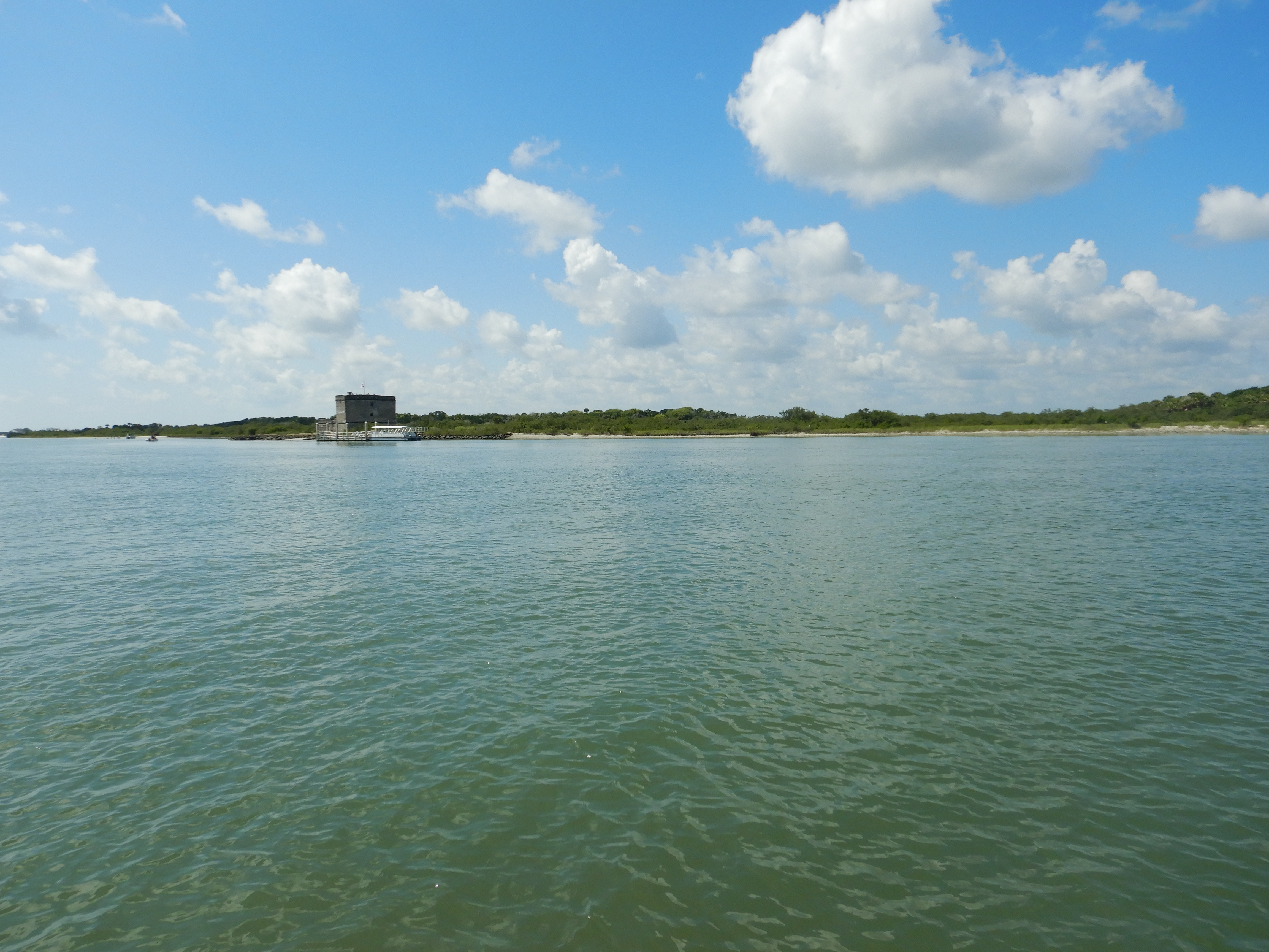 Wide shot of river with fort in the background under partly cloudy skies.