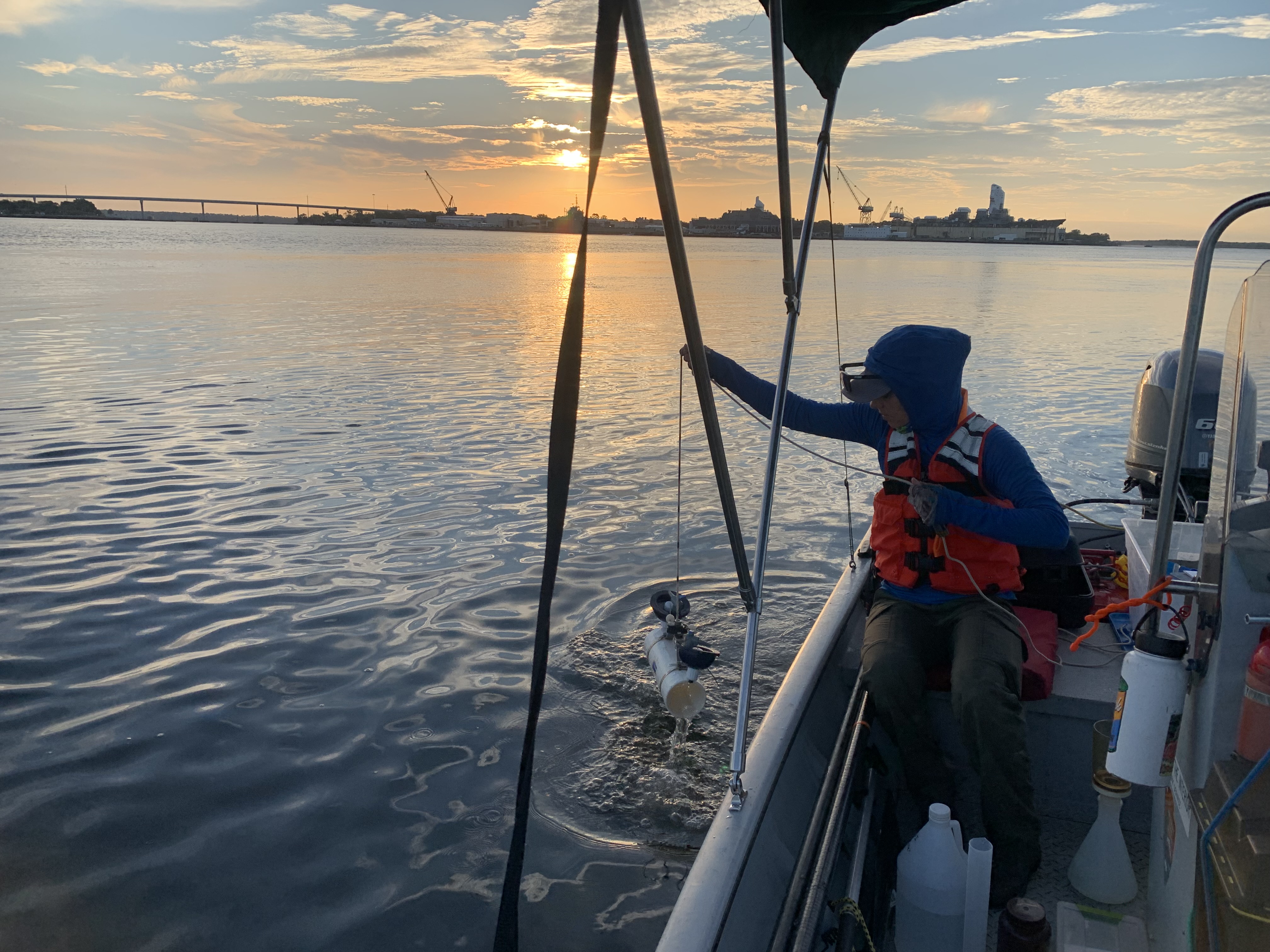 Woman in life vest holding water sampler on side of the boat