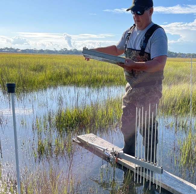 Man standing on a platform in a marsh holding a clipboard next to steel rods.
