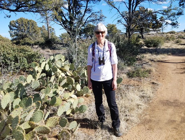 Woman stands on trail near cacti