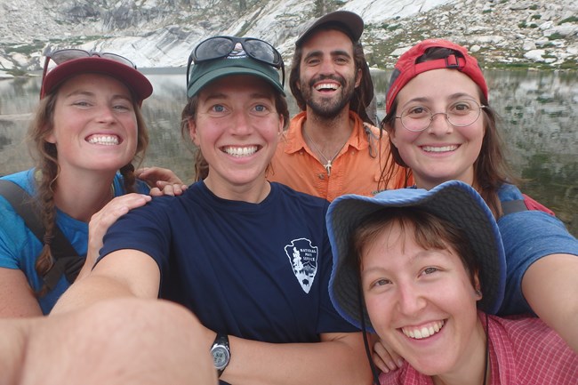 Five smiling field scientists take a selfie near a lake.