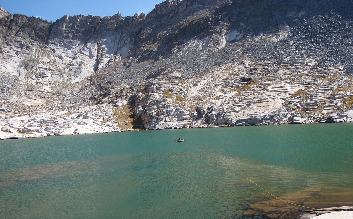 Lake sampling in Yosemite Scientist rows out to the middle of a lake surrounded by rugged rocky slopes to collect water samples.