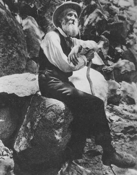John Muir, 1906 Photo of John Muir, sitting on a rock and holding a walking stick