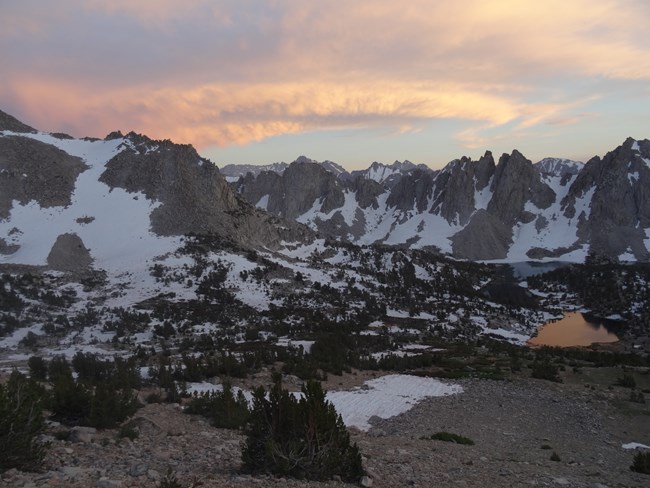 View of rugged mountain landscape and small lake, with spring snow lingering on granite peaks and slopes.