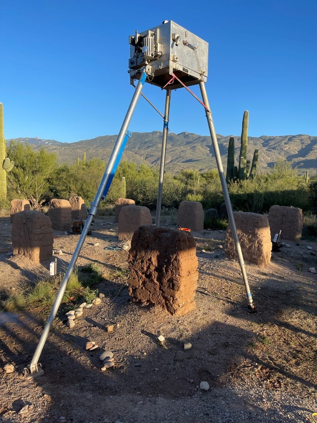 A metal box sits on a tripod centered over a small adobe wall.