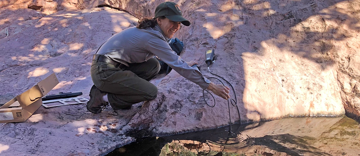 Tinaja monitoring Woman in NPS uniform crouches next to tinaja, holding a probe wired to an electronic unit.