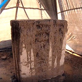 An adobe wall sits under a tent, darkened and eroded by water.