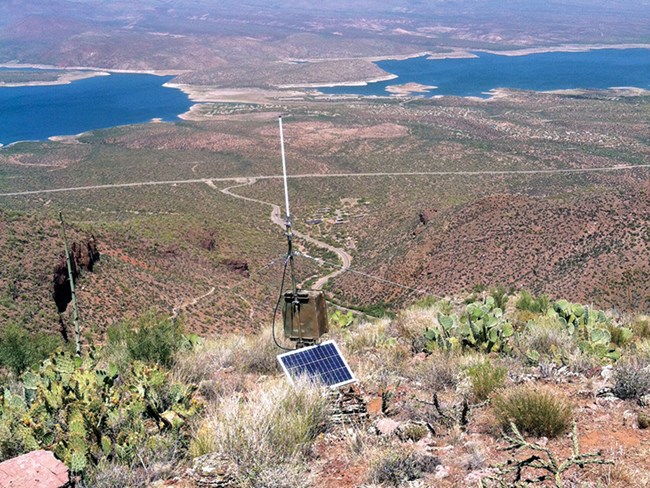 Climate station stands on mountain overlooking valley with lake