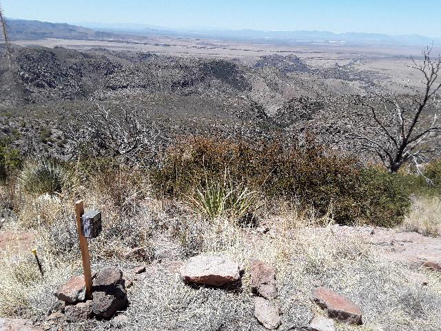 Wildlife camera on post on a brushy hillside, desert mountains in background. Wildlife camera on post on a brushy hillside, desert mountains in background.