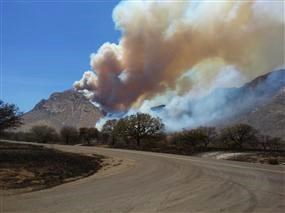 Smoke plume rises in desert mountain landscape near road