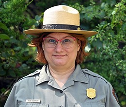A National Park Service employee shown from the shoulders up wearing a uniform shirt with badge and a flat hat.