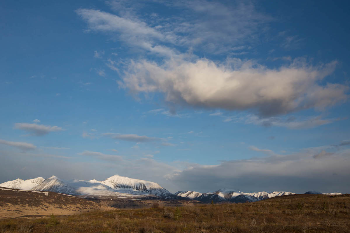 clouds hang over brown tundra with snow covered mountains in the background