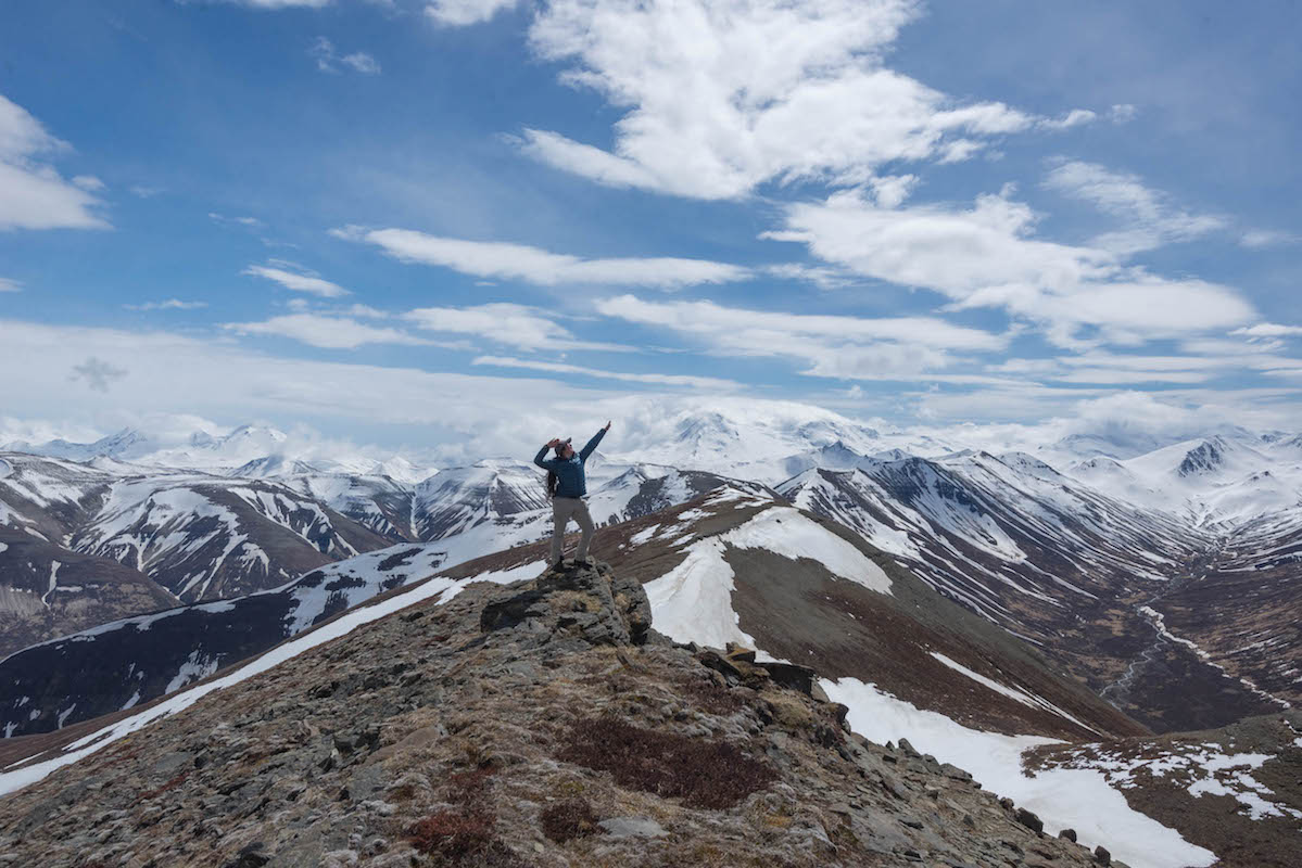 Mountain peaks surround a person standing on a summit