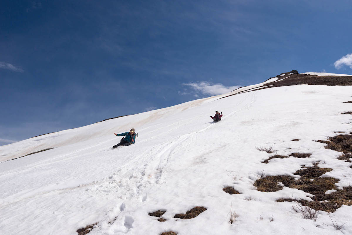 Two people slide down a snow covered slope