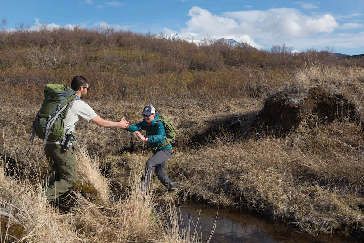 A man helps a woman cross a stream