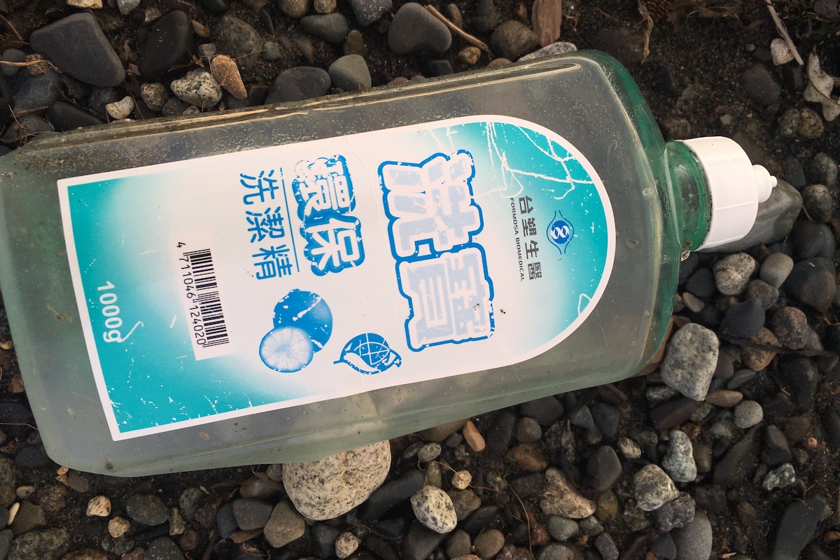 A plastic soap bottle on a rocky beach. 
