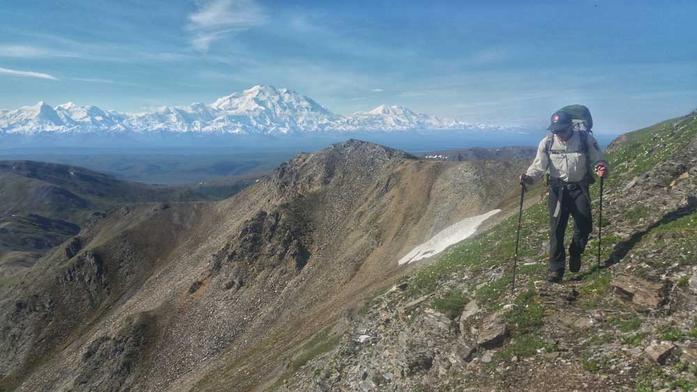 a ranger hiking on a mountainside, with a huge snowy mountain in the distance