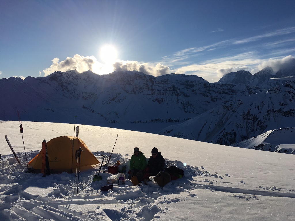 Early season training Two climbers sit outside a tent on a snowfield overlooking distant mountain peaks