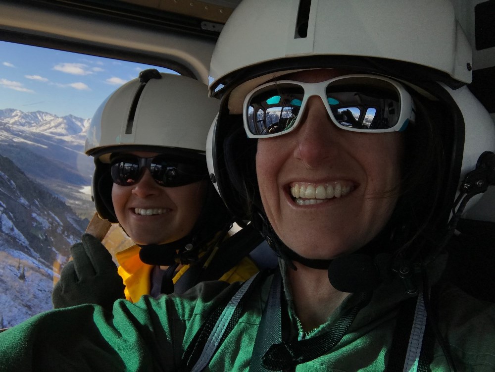 Two women fly through mountainous terrain in a helicopter