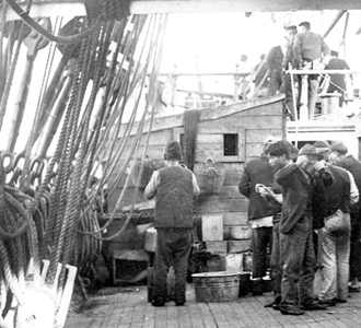 Workers aboard a sailing ship eating on deck.