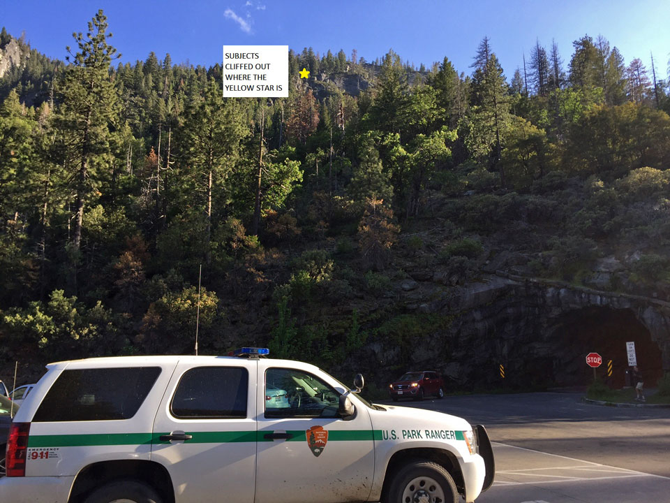 Photo of a cliff, with ranger vehicle in foreground and spot marked a few hundred feet above where hikers were stuck