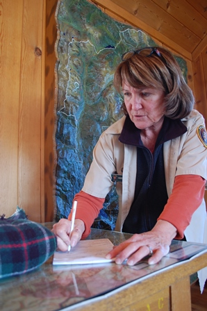 Volunteer Karen Morse logs a lost scarf in the Wilderness Office. (NPS Photo / Will Sunderland) Female volunteer looking at colorful scarf.