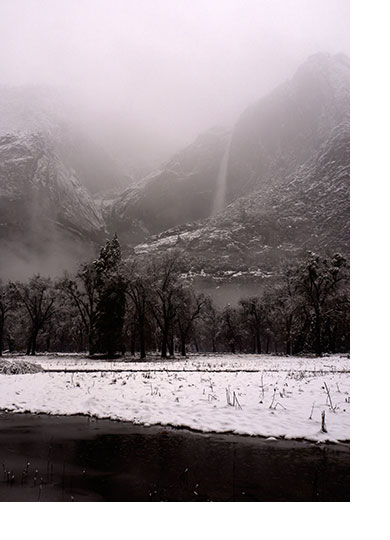 Snow falls over a river with a waterfall in the background