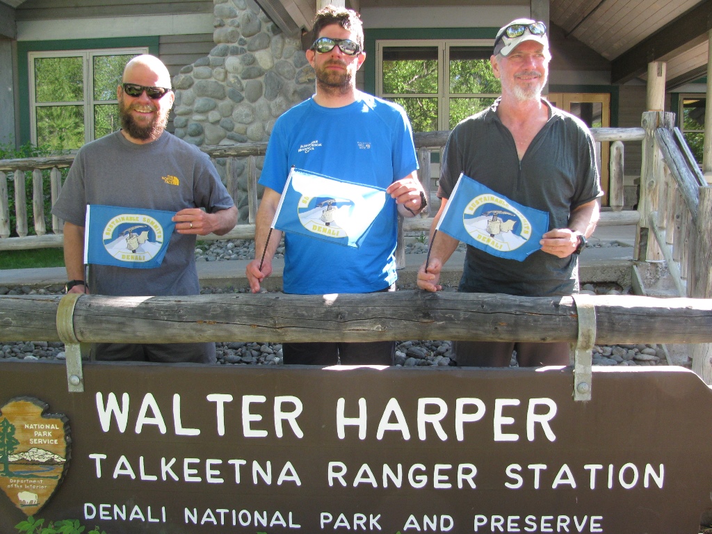 A three-person climbing team displays their Sustainable Summits flag