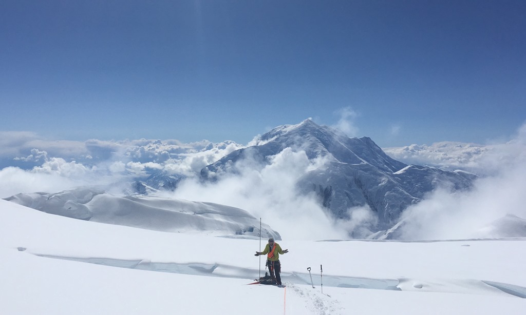 A confused climber stands in front of a crevasse, Mount Foraker in the backdrop