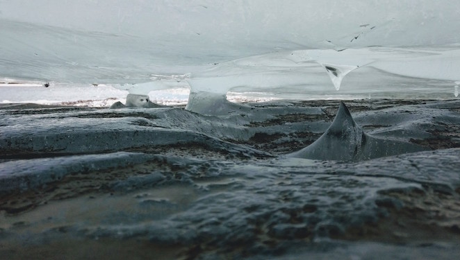 A slab of ice sites inches above the mud, creating a miniature ice-cave