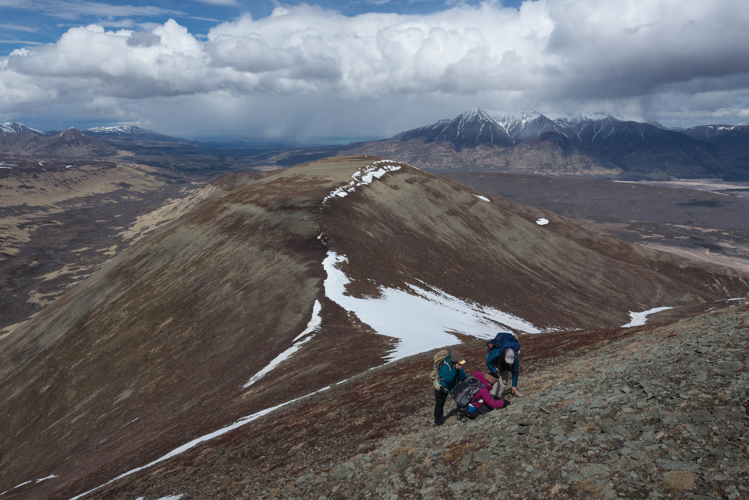 Three people bend inspect the rocky ground of a mountain ridge