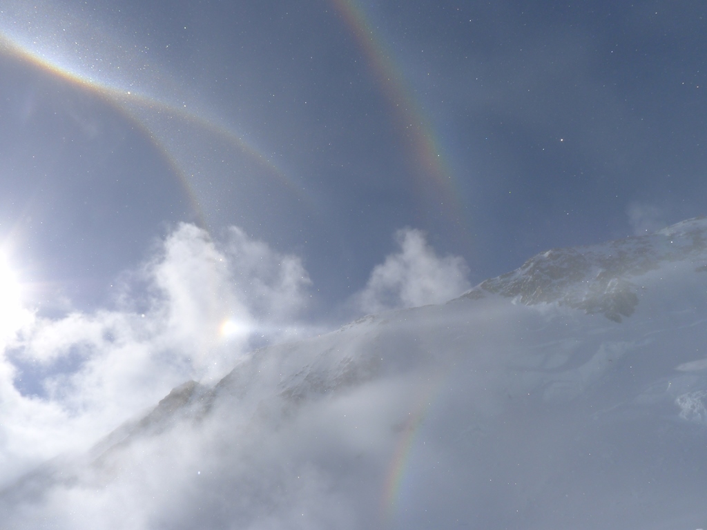 Rainbows arc and bend in front of a mountain ridge