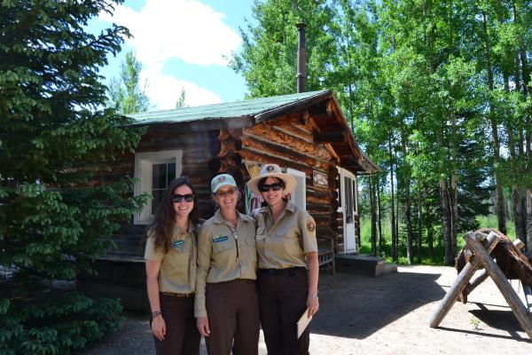 Three park volunteers looking happy in front of a cabin at Holzwarth Historic Site