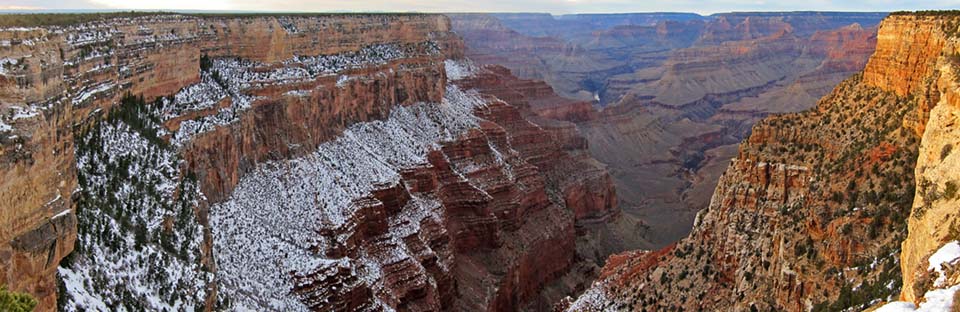 Scenic view from the Abyss, an overlook that is tucked in a bay, at the top of a drainage. There is snow on the sheer east-facing cliffs on the left. On the right the yellow glow of sunset lights up the canyon walls.