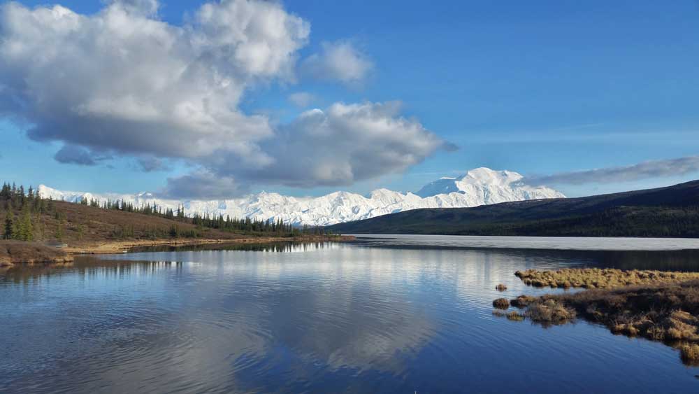 a lake reflecting some of a snowy mountain range in the distance