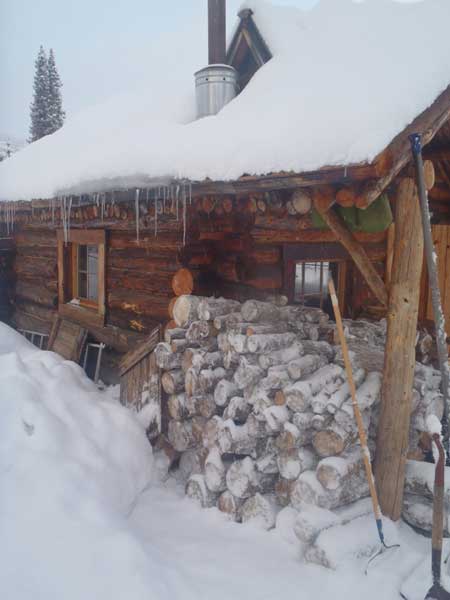 firewood stacked outside a log cabin and covered in snow