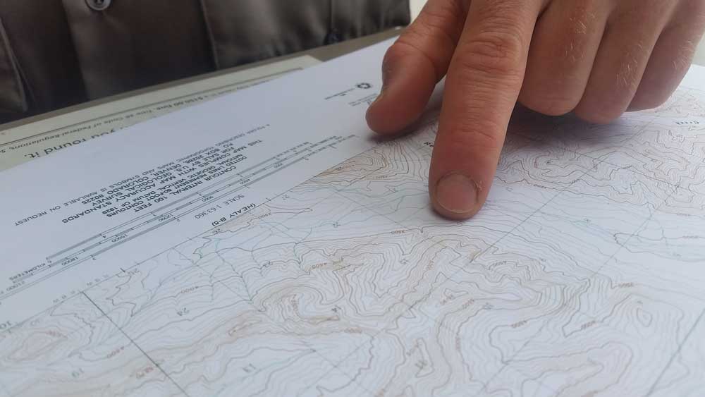 person reading a map closure of a person pointing on a topographic map