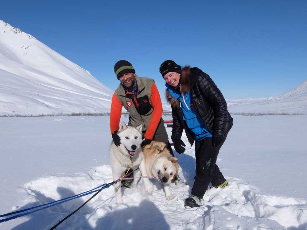 lonnie man and woman petting sled dogs in a snowy landscape