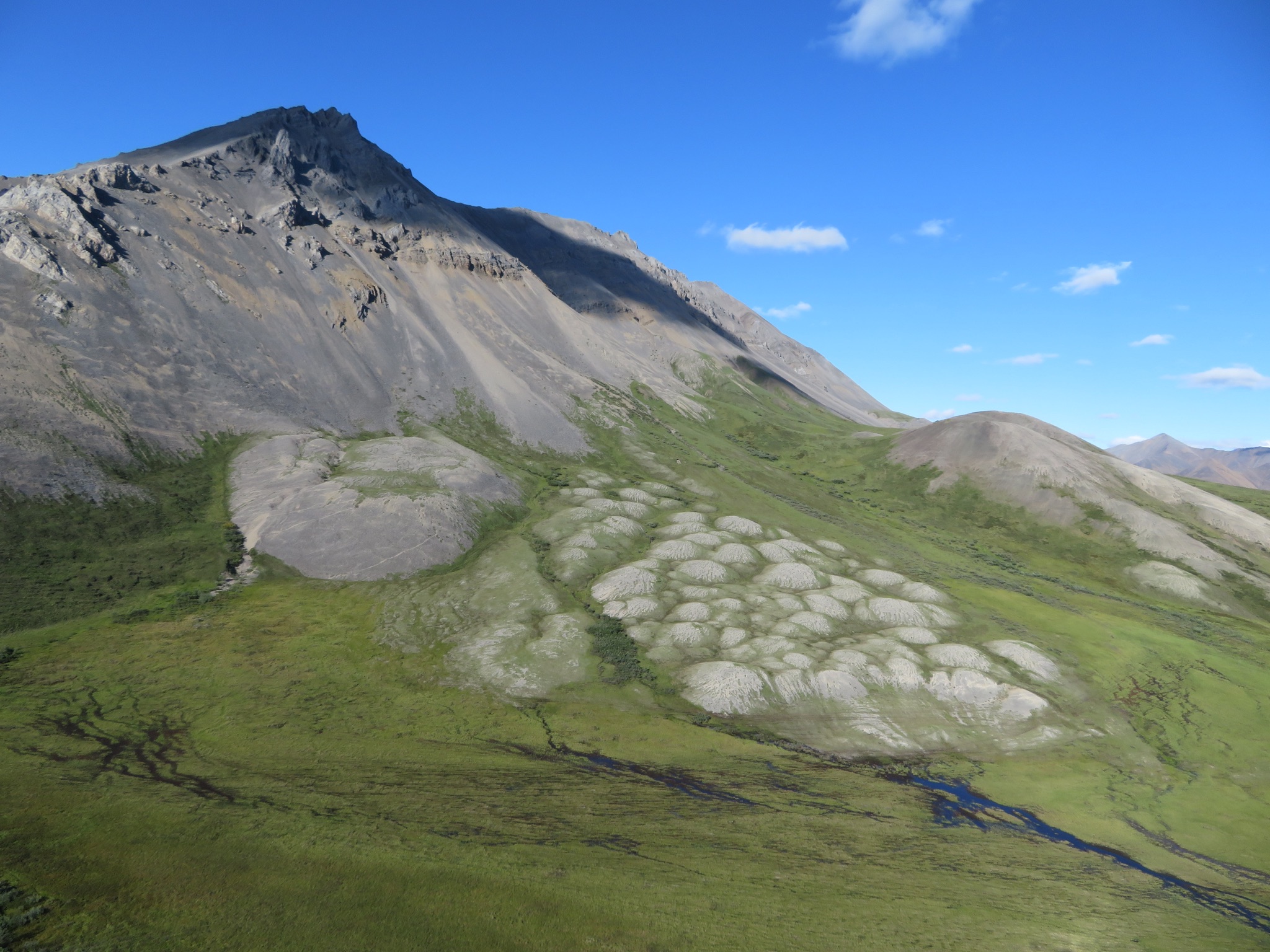 Aerial shot of mountains and green tundra against a blue sky in Noatak National Preserve.
