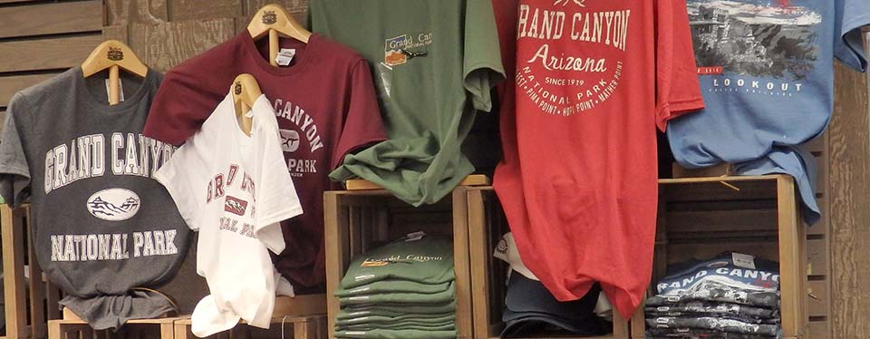 A number of colorful t-shirts hanging above a shelf that has folded stacks of the shirts on display.