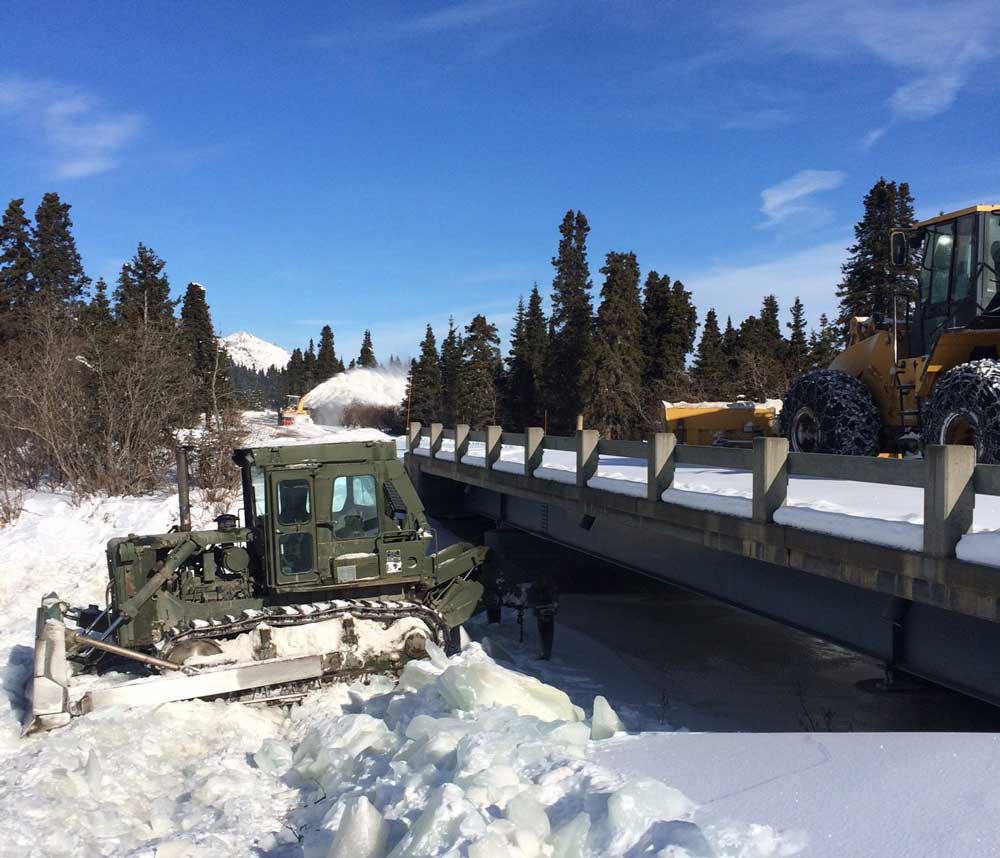 Ice Ripping a green bulldozer ripping up sheets of ice below a bridge