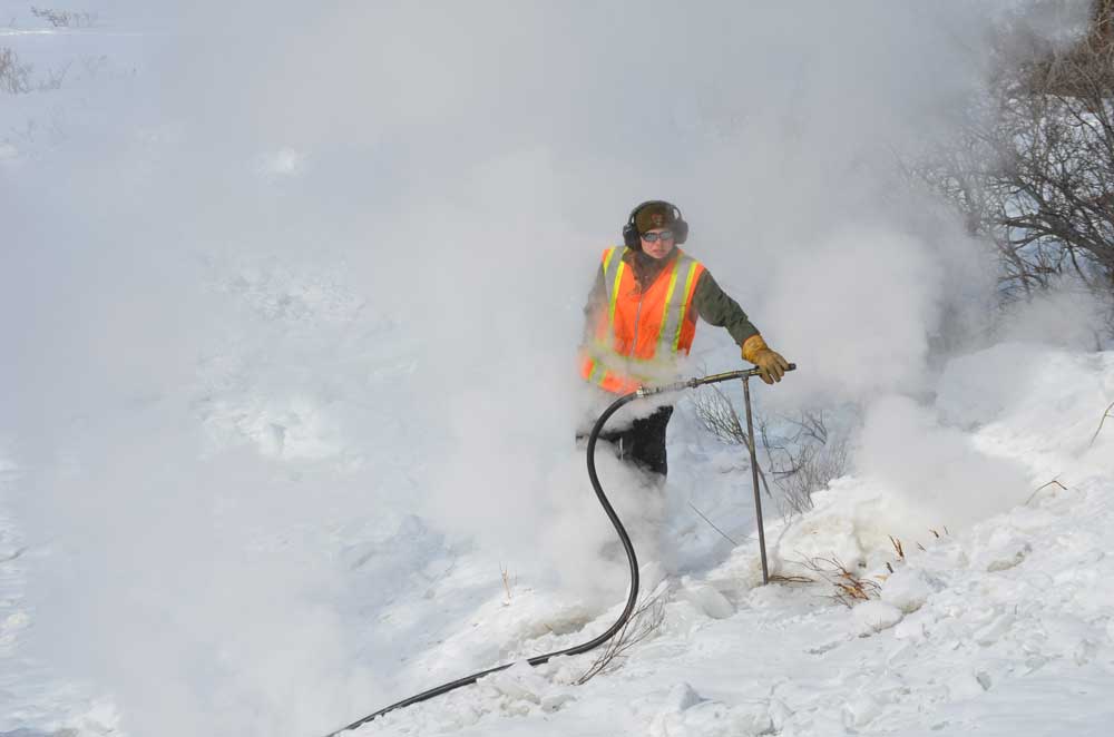 culvert steaming a woman in an orange safety vest and winter clothing surrounded by steam
