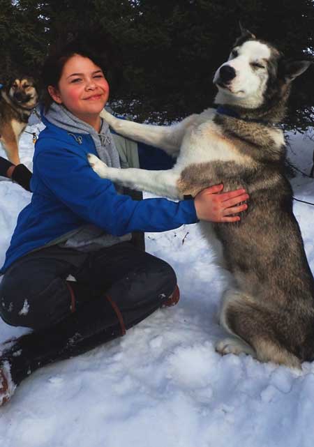 a teenager and a sled dog sitting in the snow