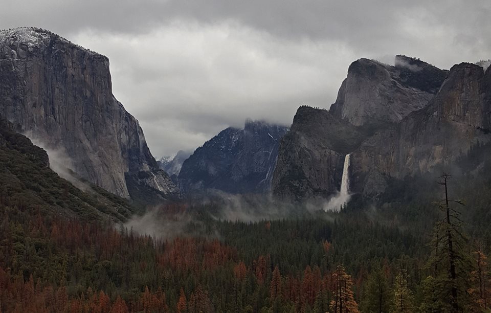 Tunnel View and Bridalveil Fall during January 2017 flood Glacially carved valley with soaring cliffs on each side. Waterfall rushing down the southern side. Rain clouds in the sky.