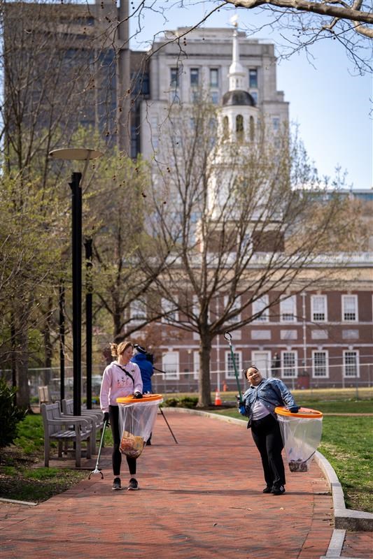 Two volunteers holding trash bags with Independence Hall in the background.