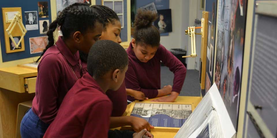 Color photo of four school children looking down at a puzzle on the desk. Color photo of four school children looking down at a puzzle on the desk.