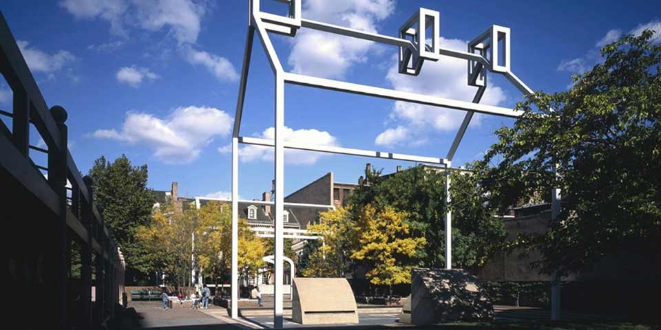 Color photo showing 3D steel house frame set in courtyard surrounded by foliage.